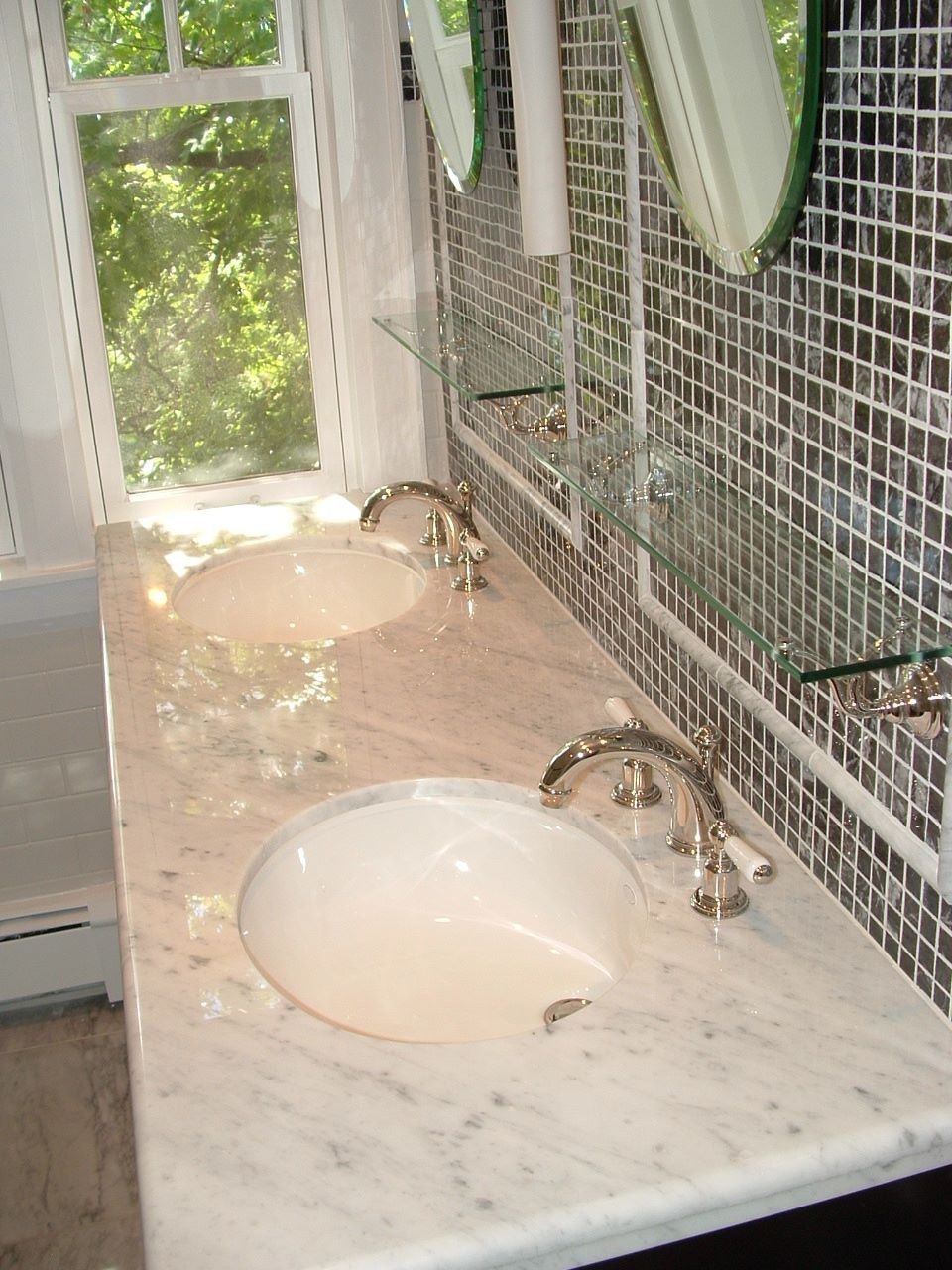Bathroom vanity with two sinks, marble countertop, mirror, and sunlight through a window.