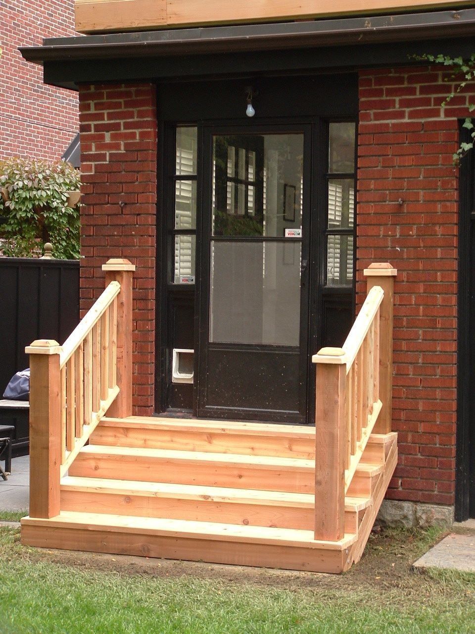 Front porch with wooden steps and railings leading to a black front door on a brick house.