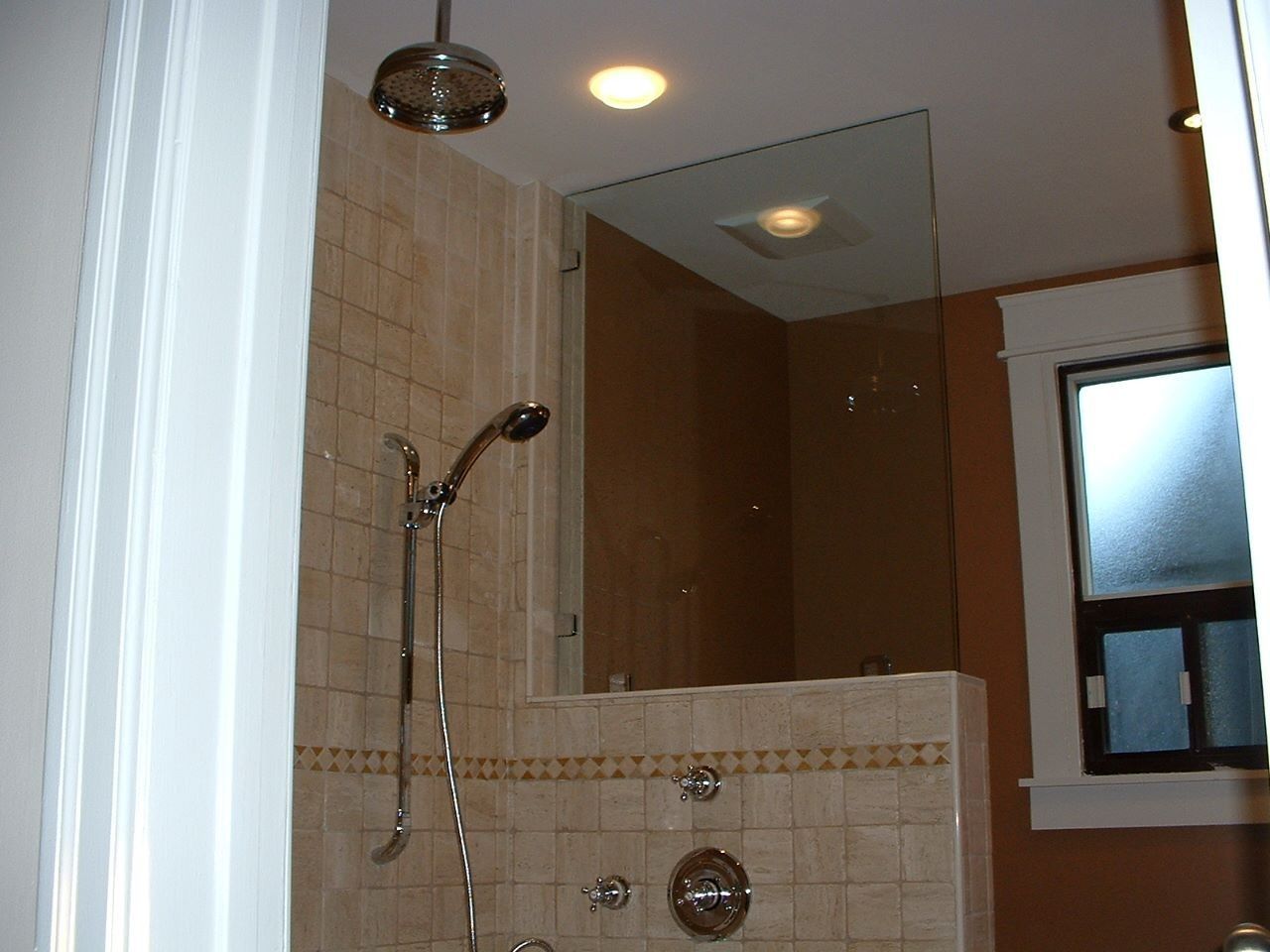 Small tiled bathroom with a shower, chrome fixtures, and a window.