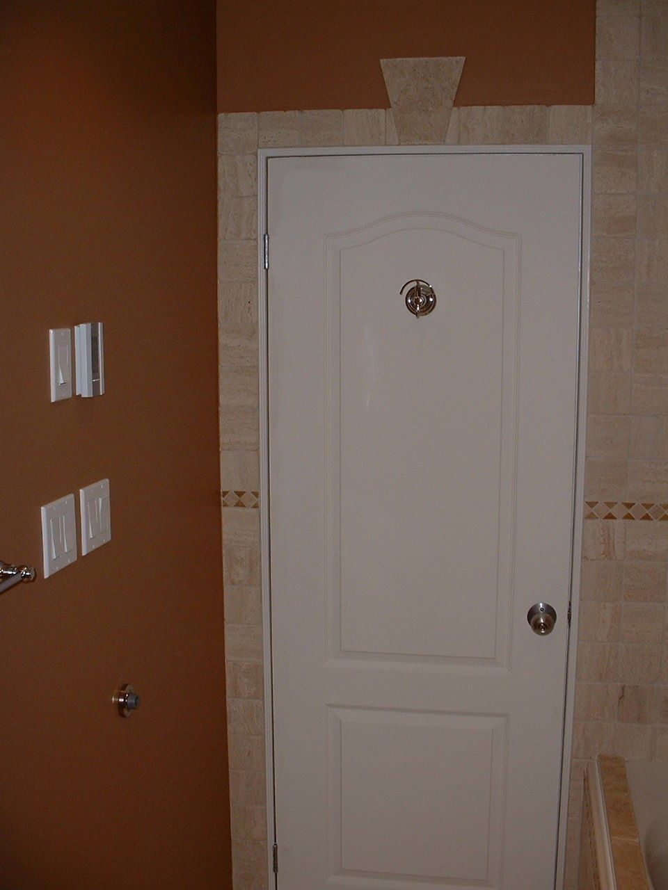 White interior door with a peephole in a hallway, beside tan tiled walls and orange paint.