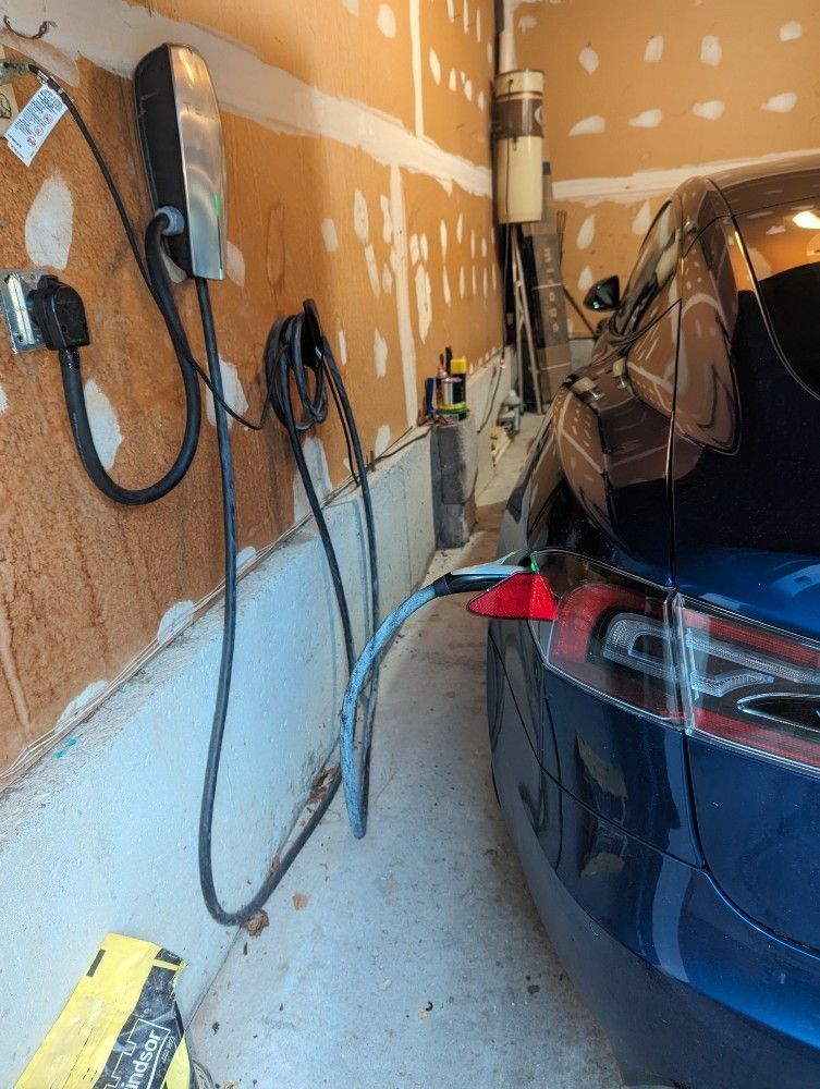 Blue car in a garage with a wall-mounted charger and cables beside it