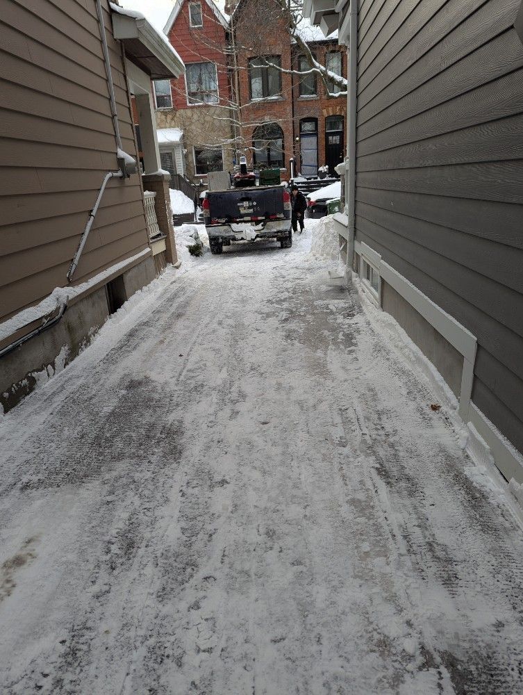 Snowy alley between buildings with a parked black truck at the far end.