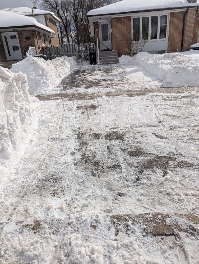 Snow-covered driveway and walkway cleared toward a brick house after a snowfall
