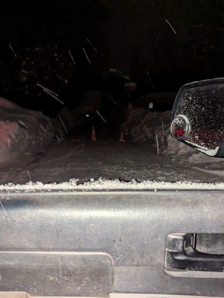 Snowy nighttime view from a car window, with falling snow and a side mirror visible.