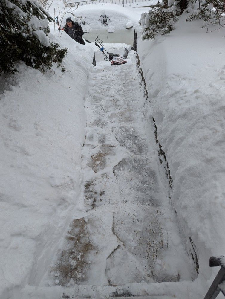 Snow-covered narrow path with deep footprints leading uphill between high snowbanks