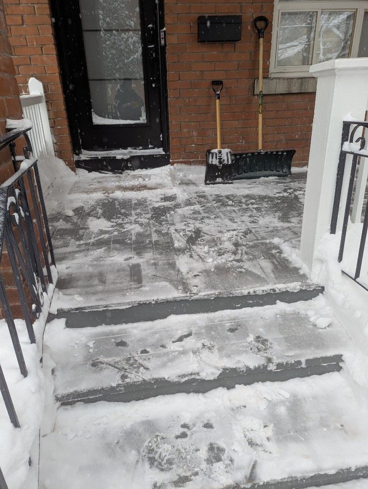 Snow-covered front steps and porch leading to a brick house entrance.