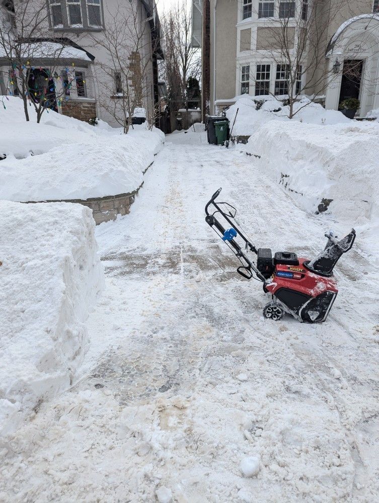 Snow-covered walkway between buildings with a snow blower clearing a path