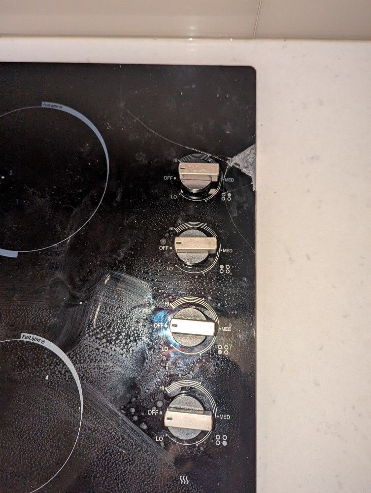 Black glass cooktop with four control knobs on the right, lightly splattered with residue.