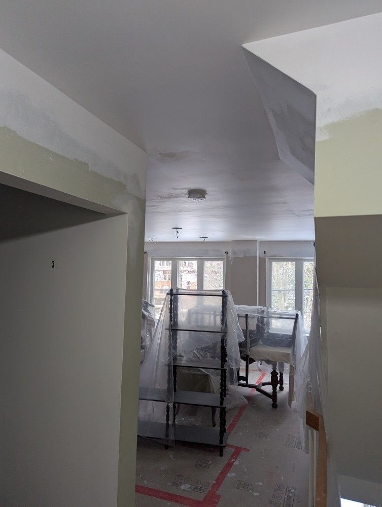Interior room under renovation with scaffolding, plastic-covered furniture, and windows at the far end.