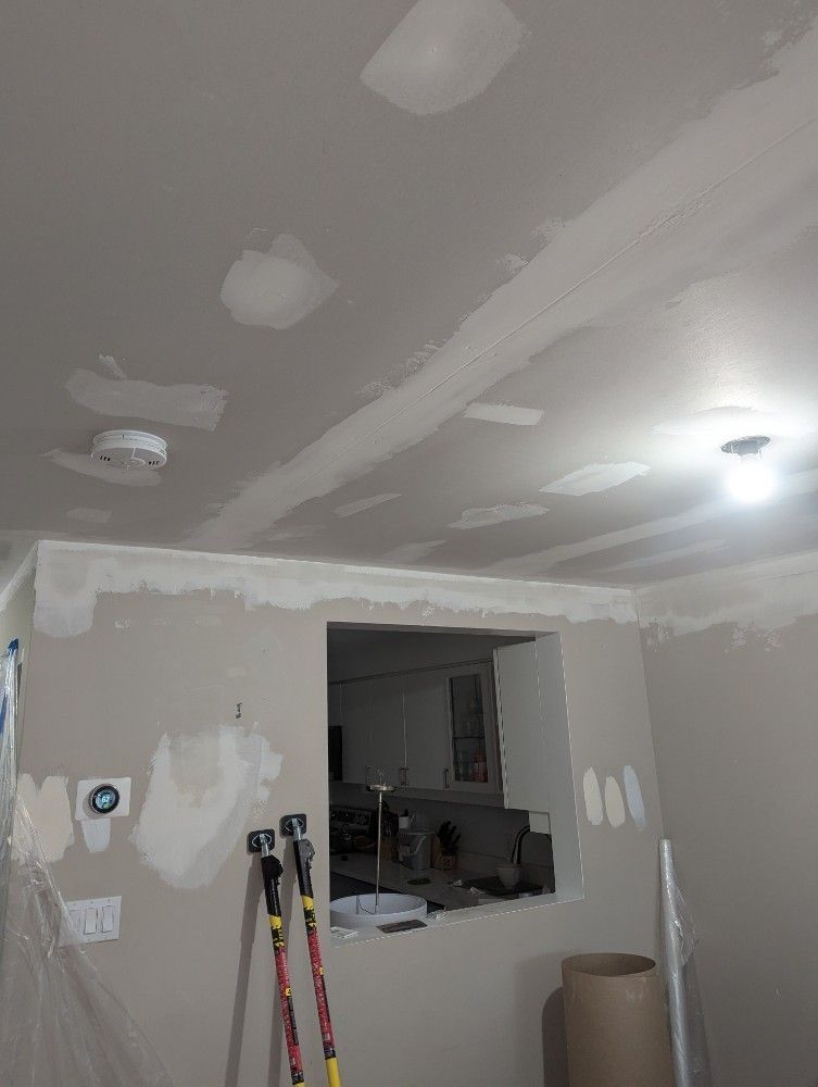 Partially finished room with drywall patches, paint tools, and a pass-through opening to another room.