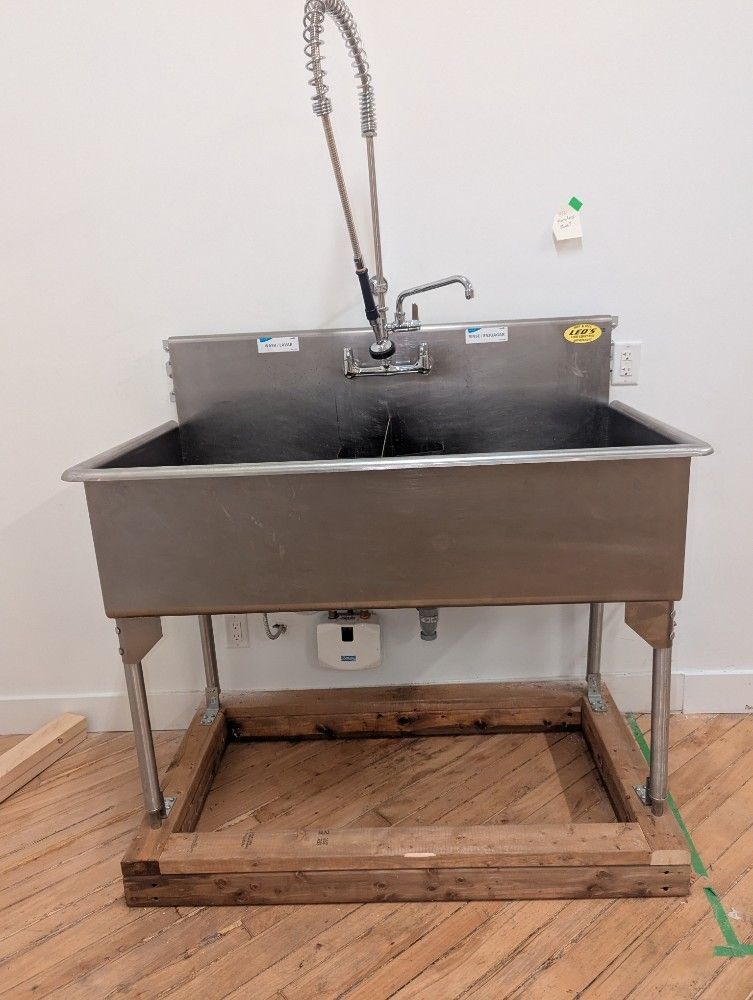 Stainless steel utility sink with faucet, set on a wooden pallet in a workshop.