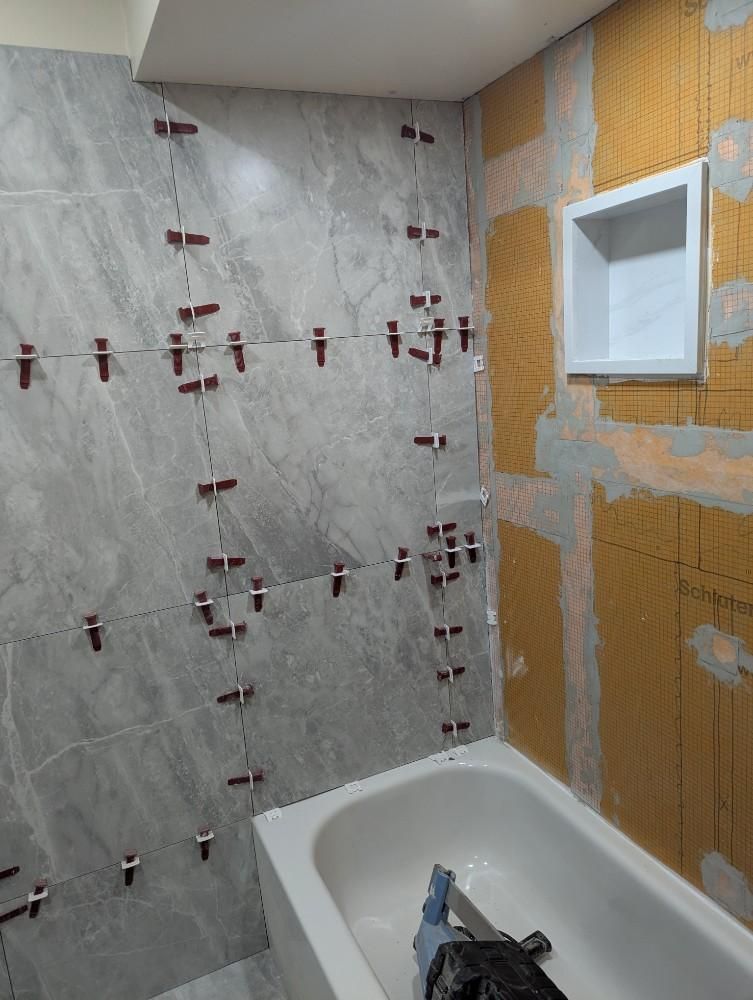 Bathroom under renovation with tiled shower wall, tub edge, and exposed wall behind a recessed niche.