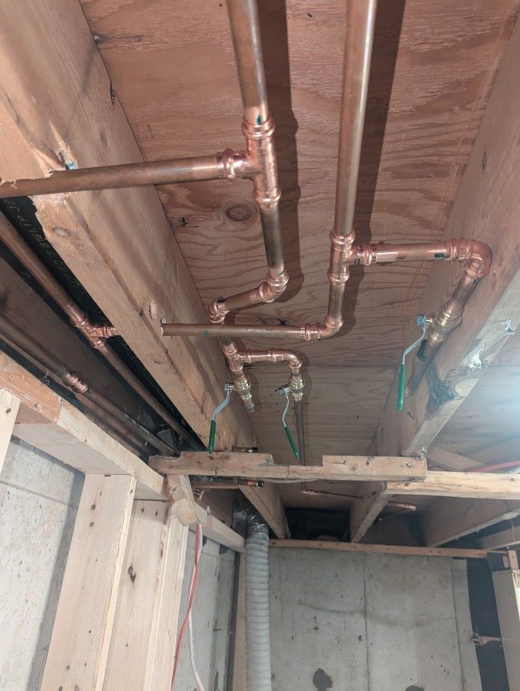 Exposed copper pipes and unfinished ceiling in a construction site basement area