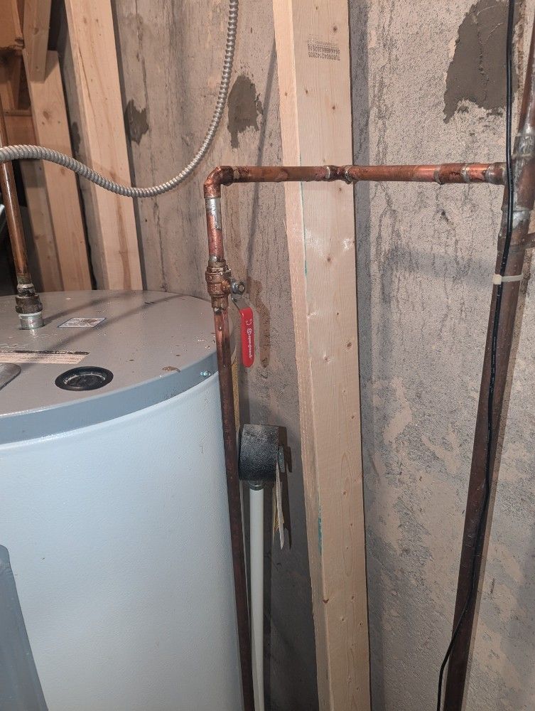 Water heater and exposed copper piping in an unfinished basement wall area