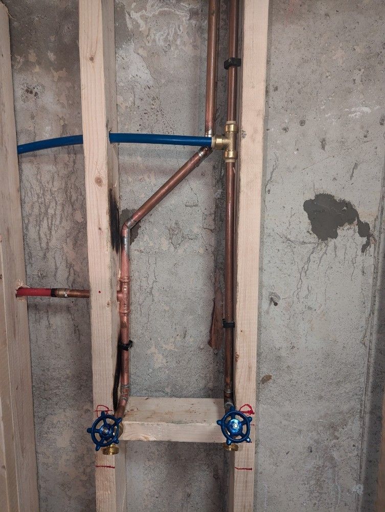Wall plumbing with exposed copper pipes, blue PEX lines, and shutoff valves in an unfinished concrete room