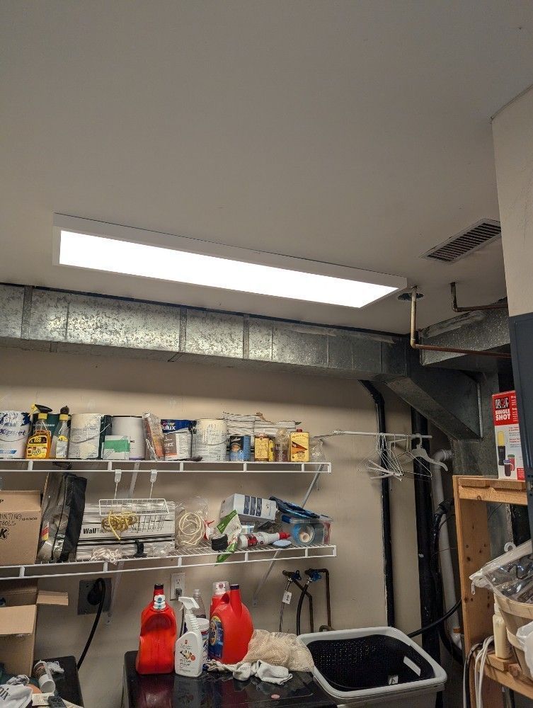 Shelves of paint cans and supplies in a workshop or garage under fluorescent light.