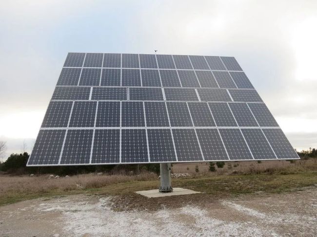 Solar panel array on a metal stand in a cloudy outdoor field.