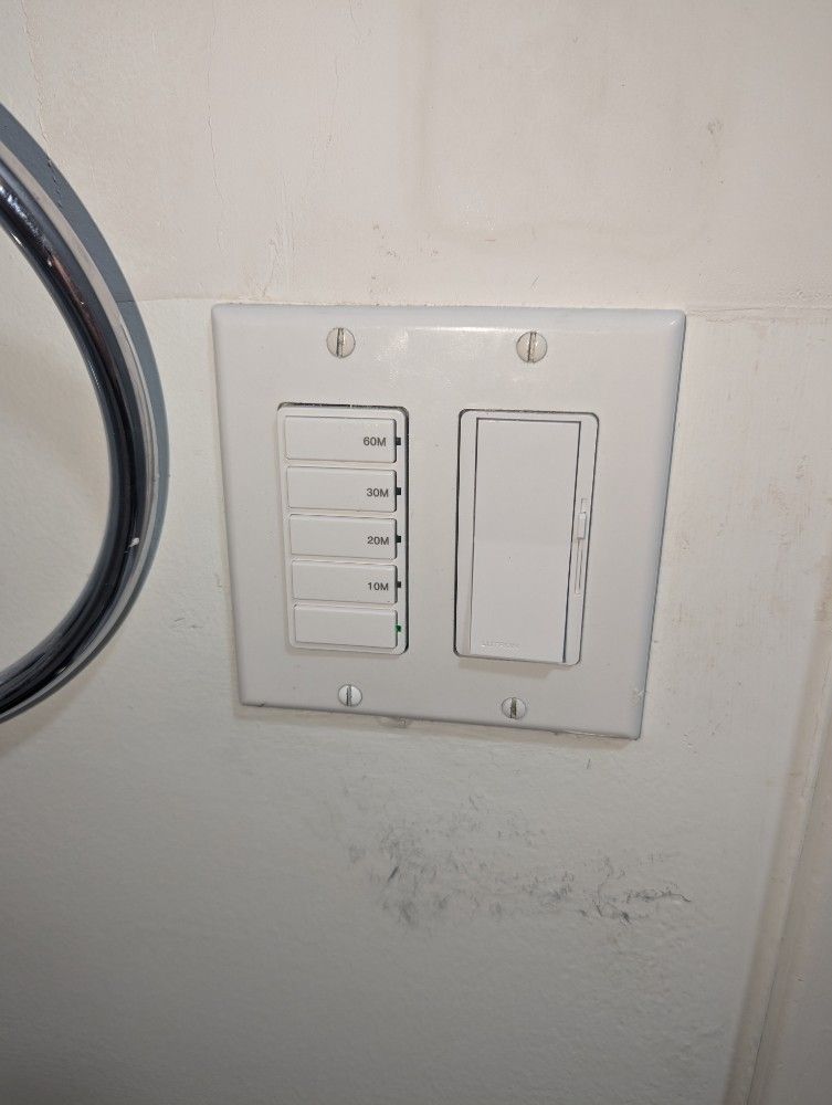 Wall-mounted switch panel with five small buttons beside a large blank switch plate on a white wall