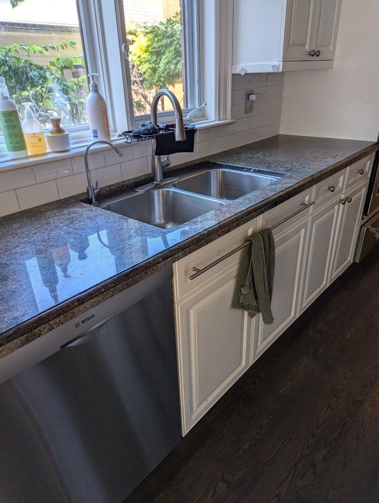 Modern kitchen sink with granite countertop, white cabinets, and a window above the faucet.