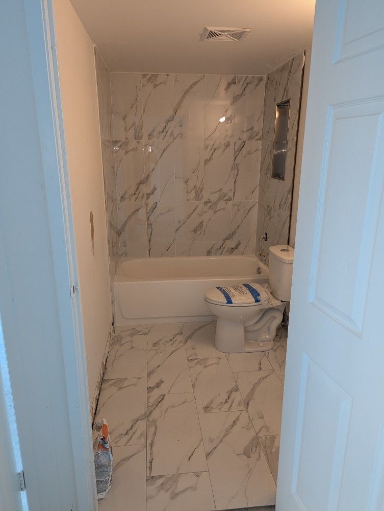 Small bathroom with marble-pattern tile, white tub, toilet, and a partially open door.