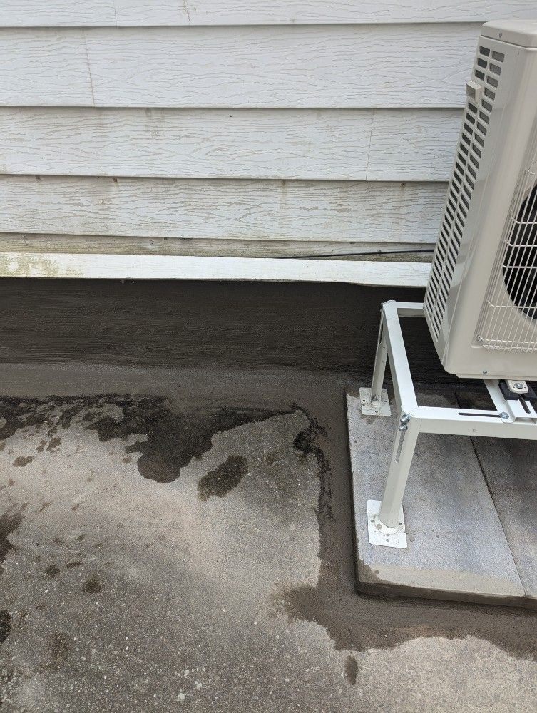 Wet concrete slab beside white house siding and an outdoor HVAC unit on a stand.
