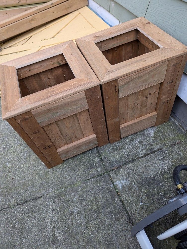 Two wooden planter boxes on a patio, each with square cutout openings on top.