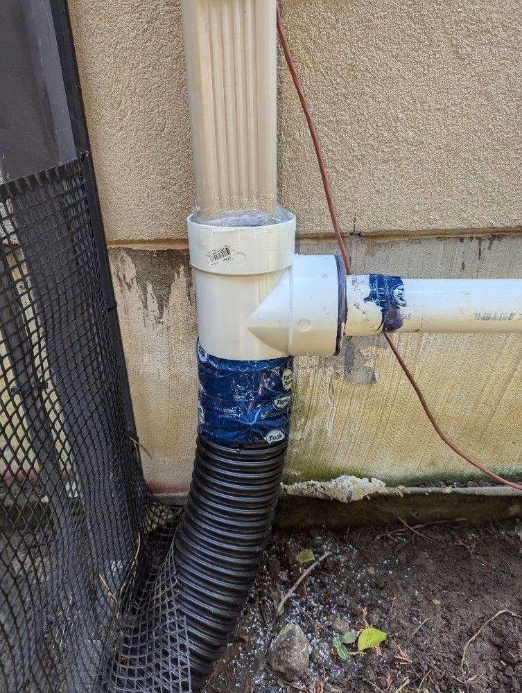 White PVC drainpipe with elbow joint and black corrugated hose beside a wall outdoors.