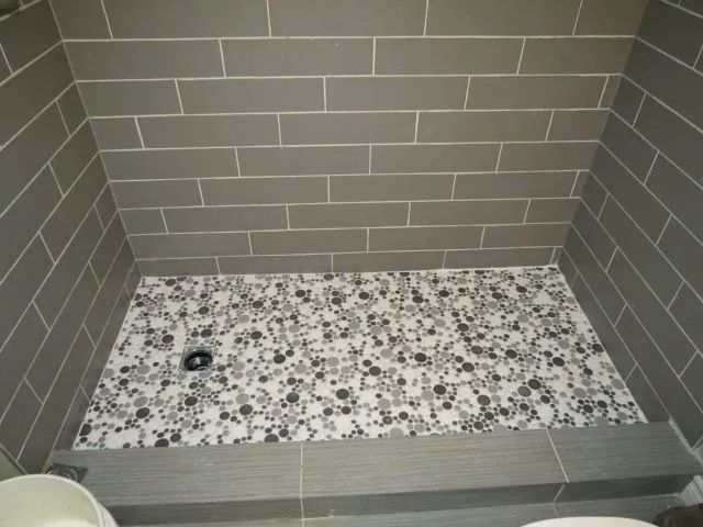 Walk-in shower with gray tile walls and a speckled stone bench or floor.