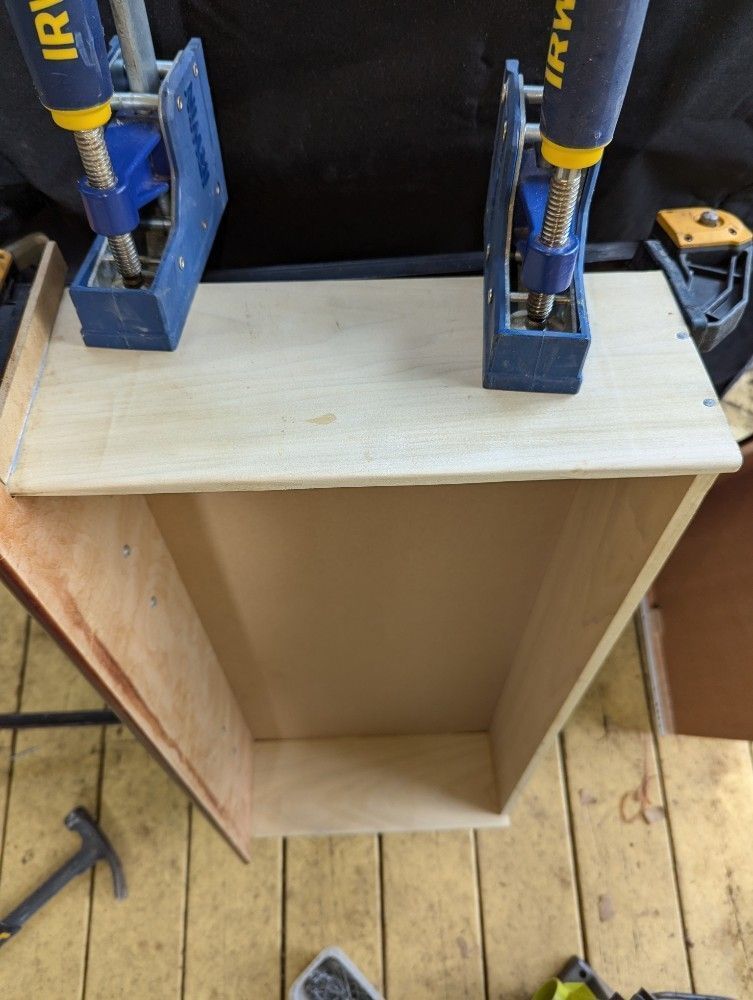 Wooden cabinet carcass being clamped together in a workshop, with two bar clamps on top.