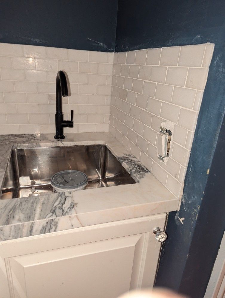 Small kitchen sink with black faucet, white tile backsplash, and blue walls.