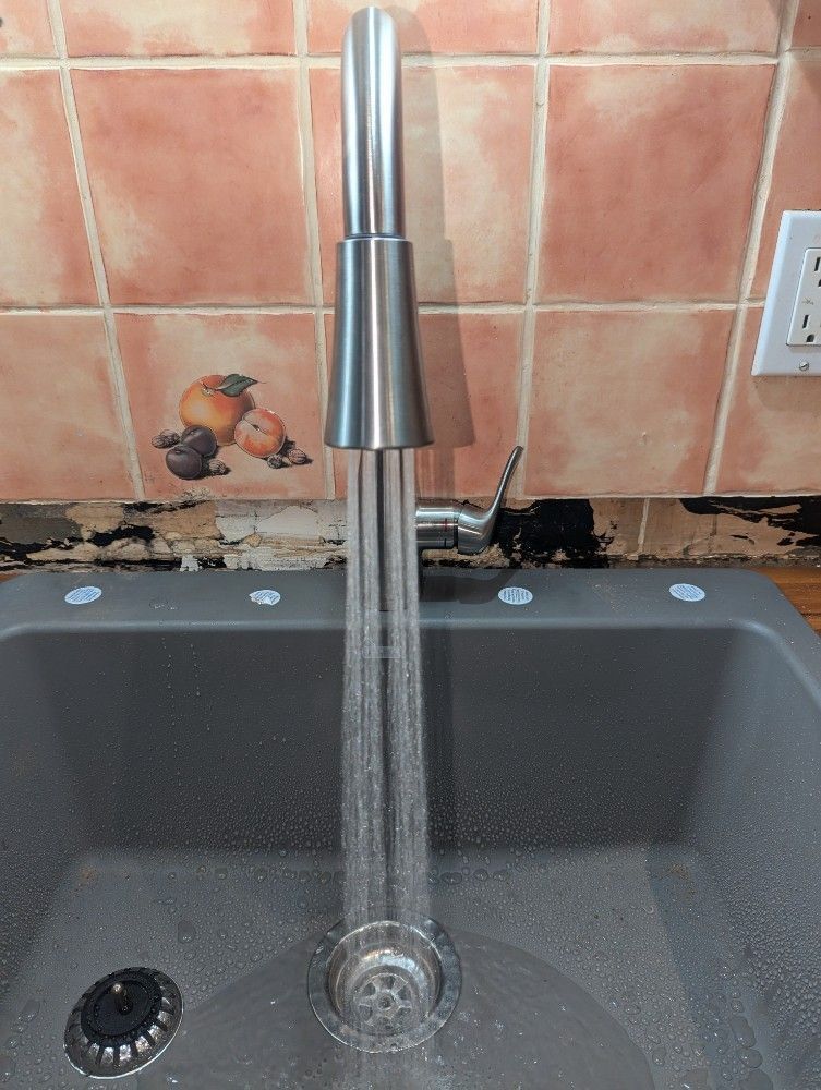 Modern kitchen faucet running water into a gray sink, with pink tile backsplash behind it