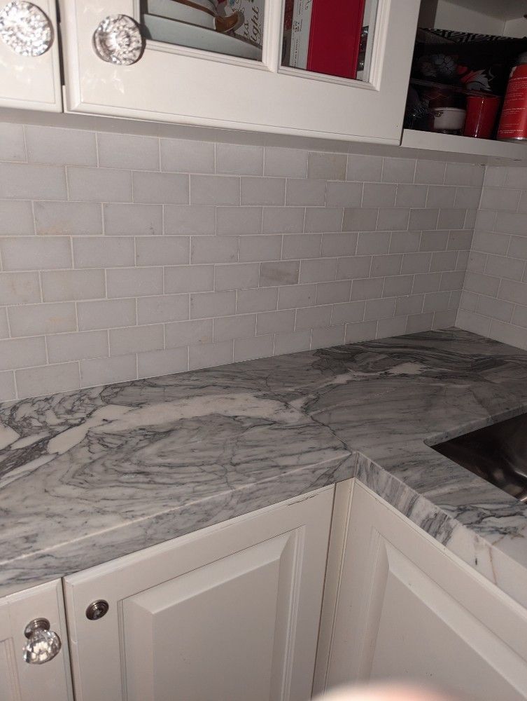 White kitchen corner with marble-look countertop, white cabinets, and tile backsplash
