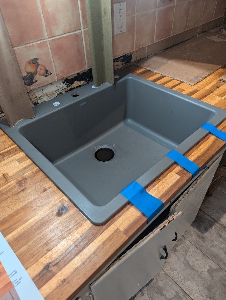 Gray sink basin installed in a wooden countertop, held in place with blue tape during installation