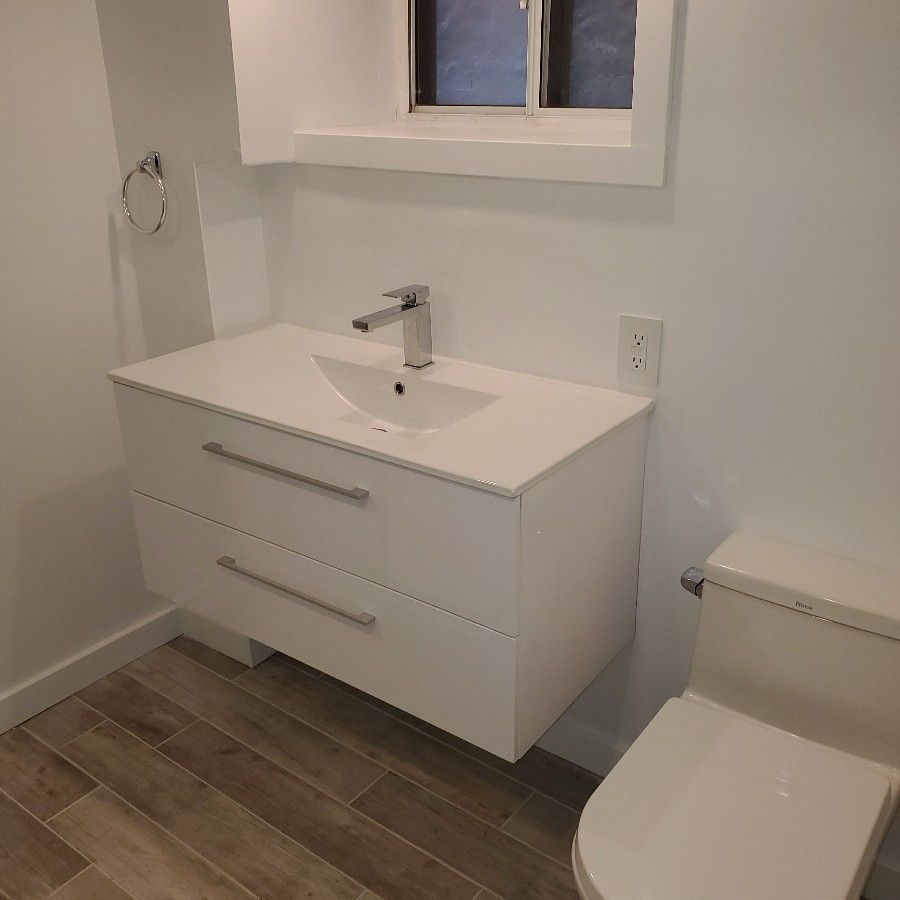 Modern bathroom with white vanity, sink, toilet, and small window above.