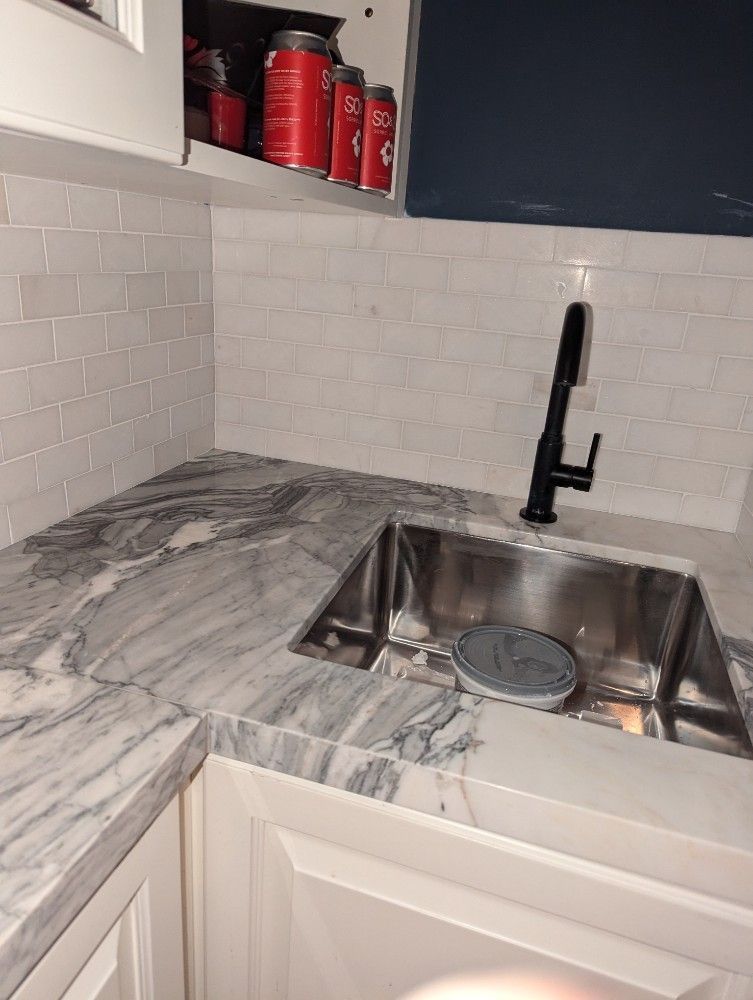 White marble kitchen counter with stainless sink, black faucet, and red containers on open shelf