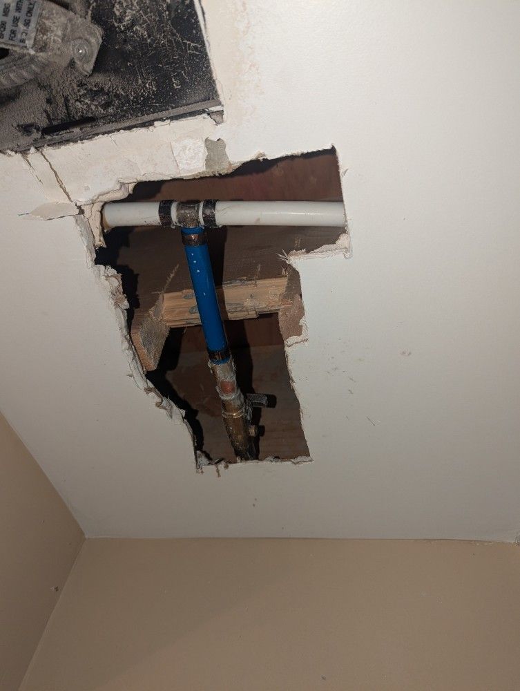 Damaged ceiling with a hole exposing pipes and a blue valve handle amid broken drywall.