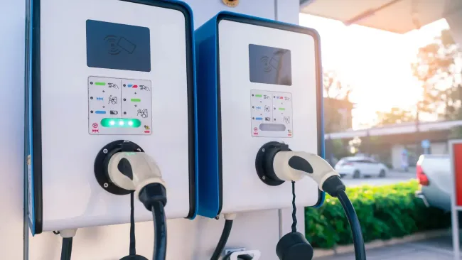 Two electric car charging stations with cables plugged in, outdoors in bright sunlight