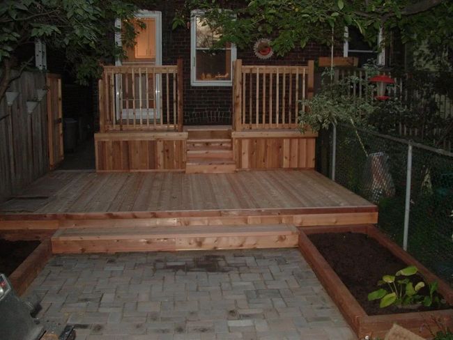 Wooden backyard deck with railing, steps, and a small paver patio below