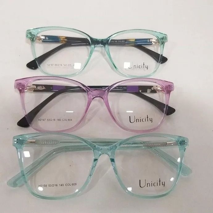 Tres pares de monturas de gafas translúcidas en verde, morado y turquesa, apiladas sobre un fondo blanco.