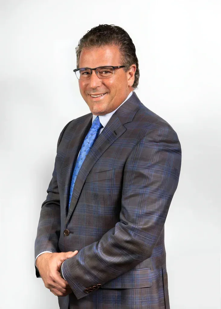 Man in a plaid suit and blue tie standing against a white background, smiling at the camera