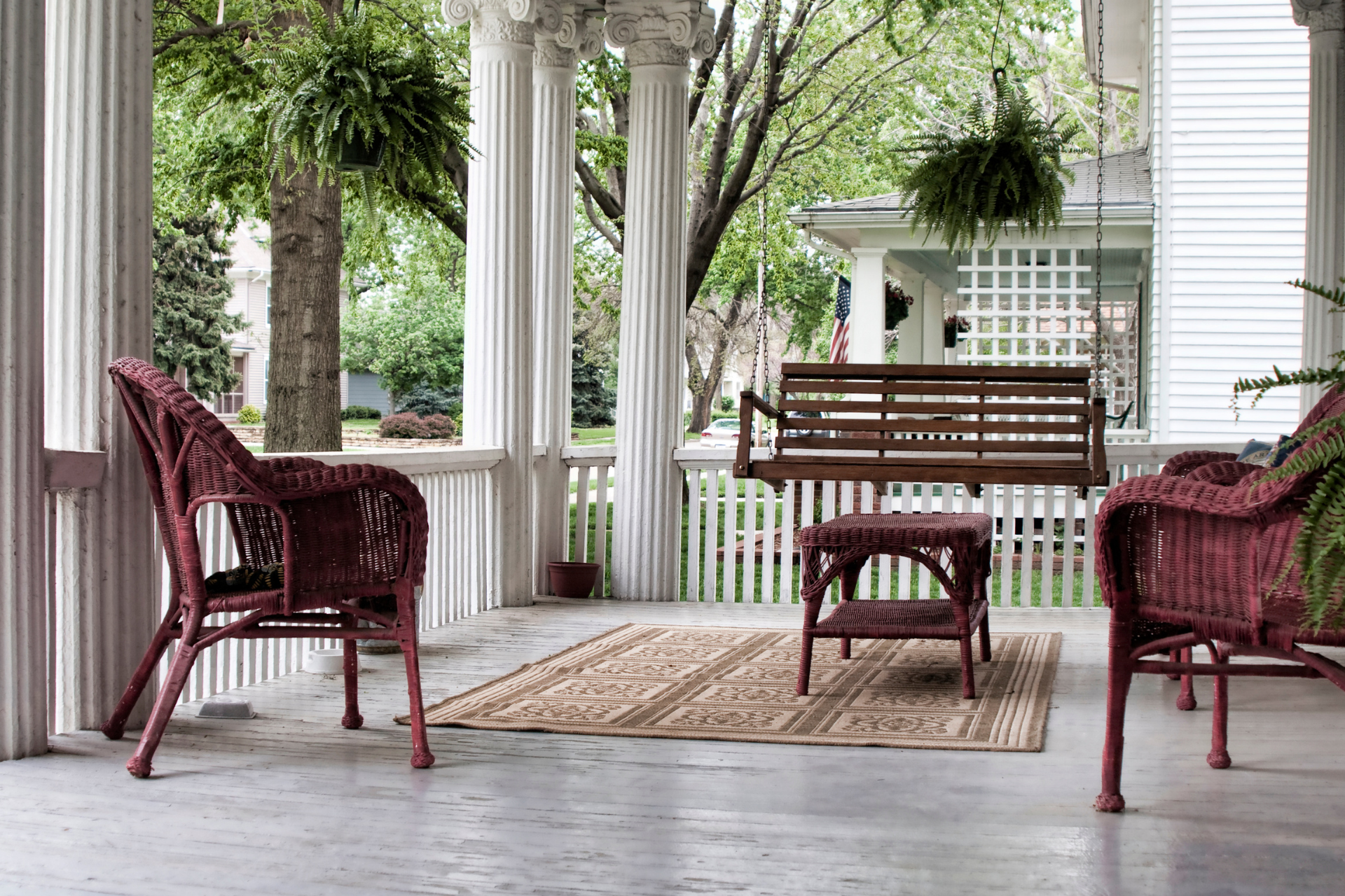 A porch with wicker chairs , a table and a swing.