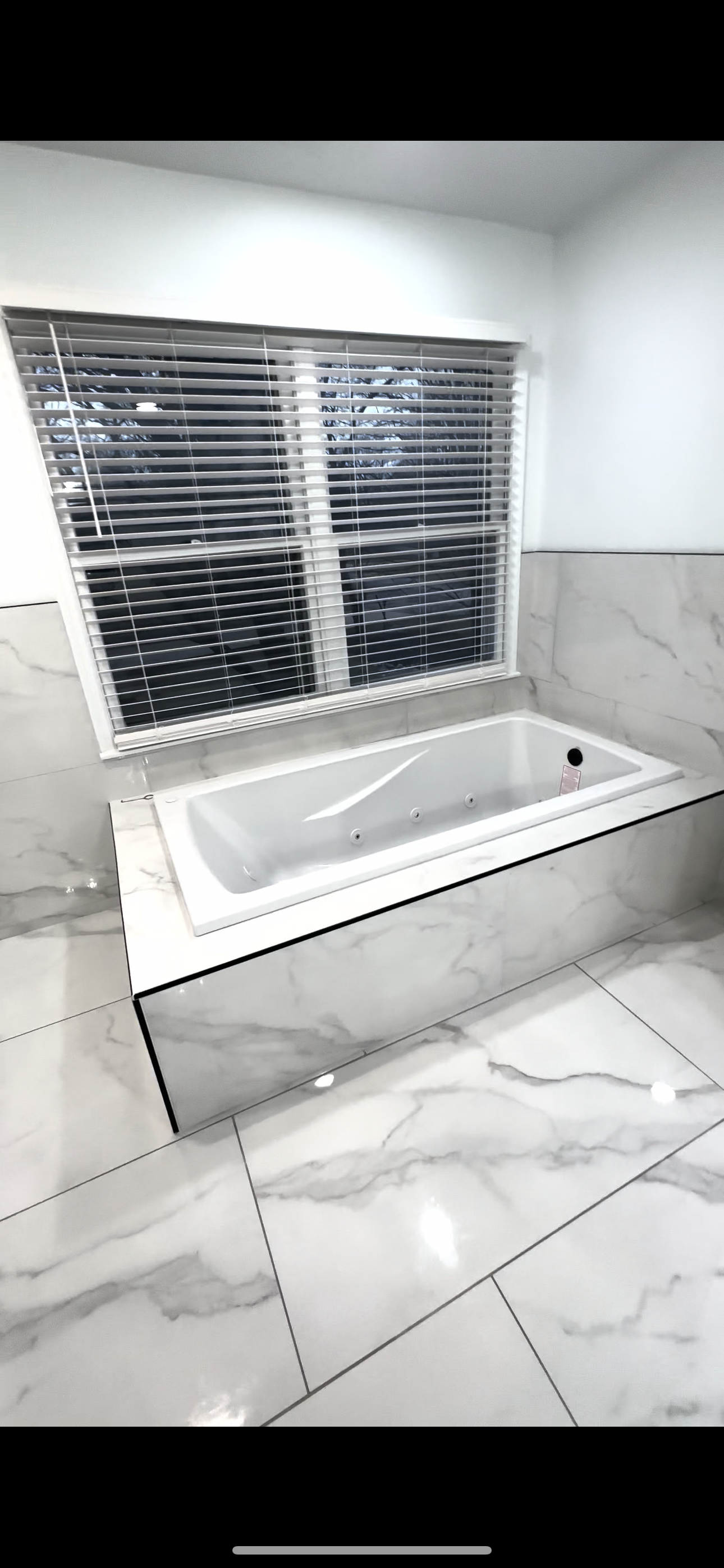 A bathroom with a bathtub and a window with blinds.