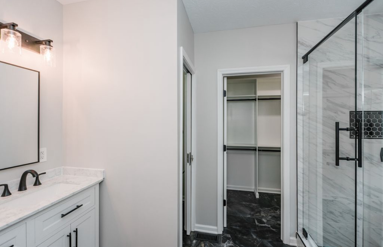 A bathroom with a sink , mirror and walk in closet.