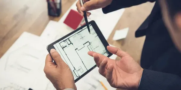 A man is using a tablet computer to draw a floor plan.