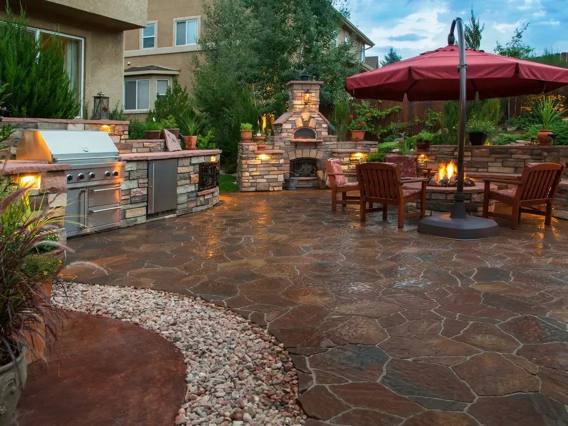 A patio with a grill , umbrella , chairs and a fireplace.