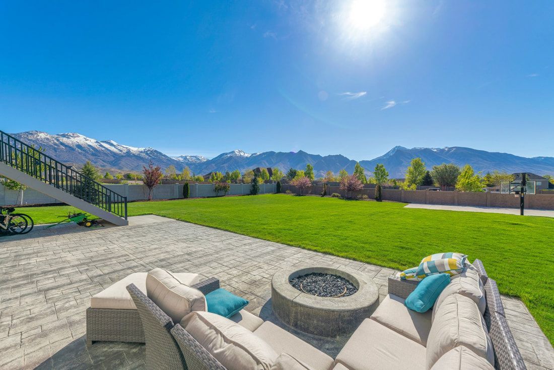 Spacious backyard patio with cozy beige sofas and cushions surrounding a fire pit. 