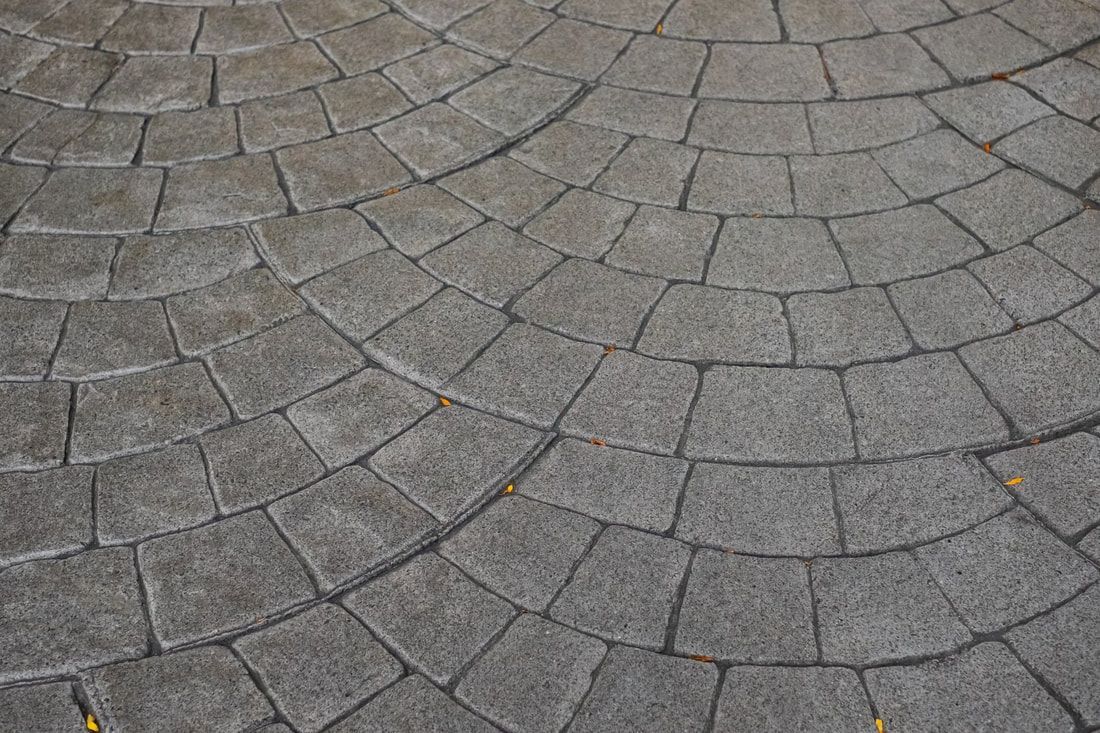 Gray cobblestone pavement forms circular patterns, with scattered small yellow leaves.