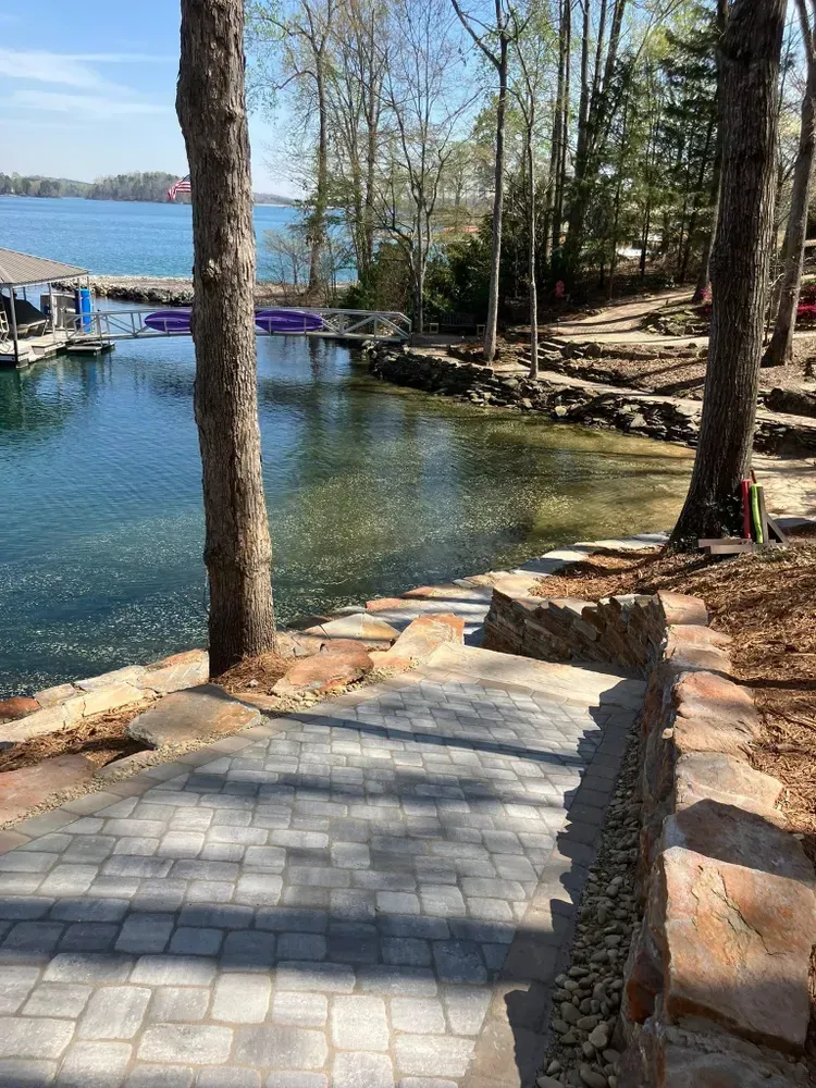 Stone steps leading to a dock on a wooded lakeshore with clear blue water and sunlight