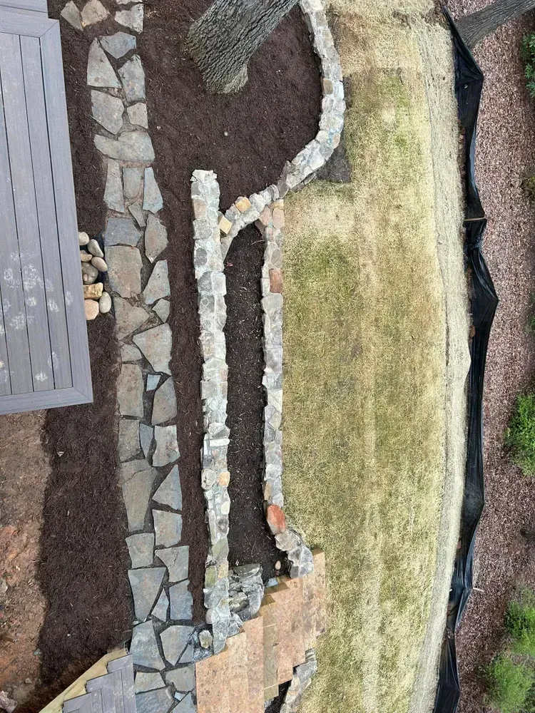 Aerial view of a landscaped garden with stone paths, dark soil, and patches of moss and gravel.
