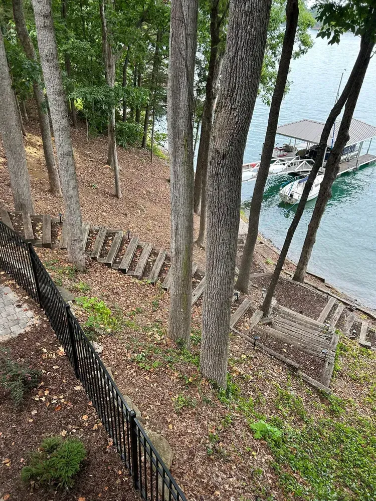 Wooded lakeshore with stone steps descending to a dock on calm water